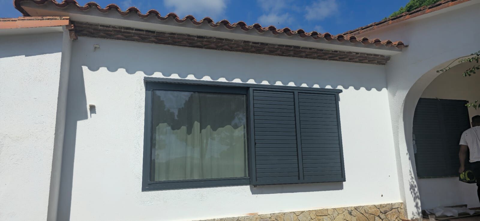 Ventana de aluminio con contraventanas oscuras en una fachada blanca