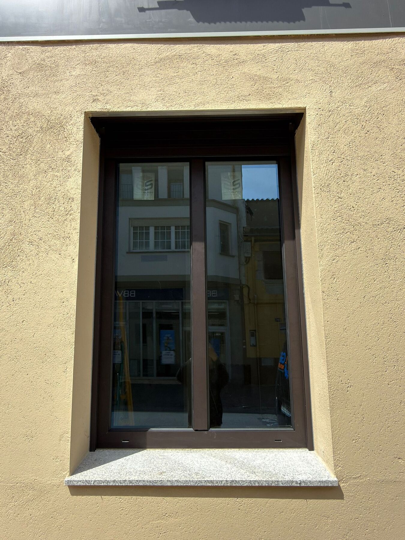 Ventana de aluminio oscura de dos hojas en una fachada de color ocre